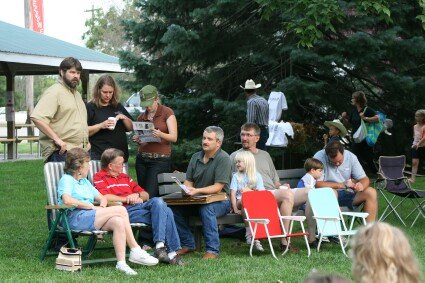 People gathered outdoors on chairs and blankets in a grassy yard, chatting during a picnic.